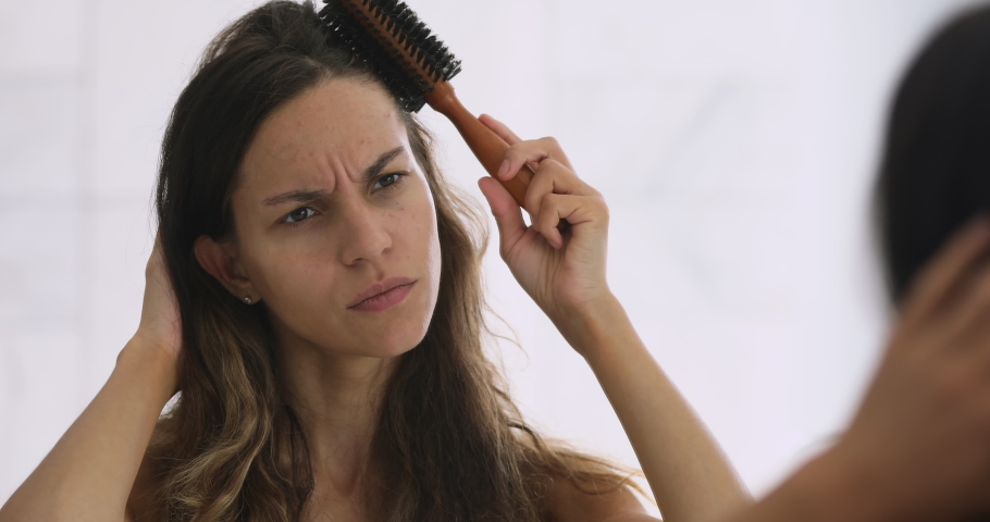 Head shot close up stressed millennial mixed race woman looking at mirror, brushing hair. Irritated annoyed young girl dissatisfied with damaged dry hair condition, hard to style, morning routine. Royalty-Free Stock Footage #1047837517