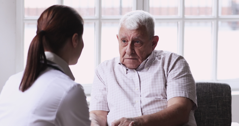 Senior elder man patient talking to caring female doctor physician caregiver at nursing home in hospital holding hands explaining well-being get support and medicare services at medical checkup visit. | Shutterstock HD Video #1047837520