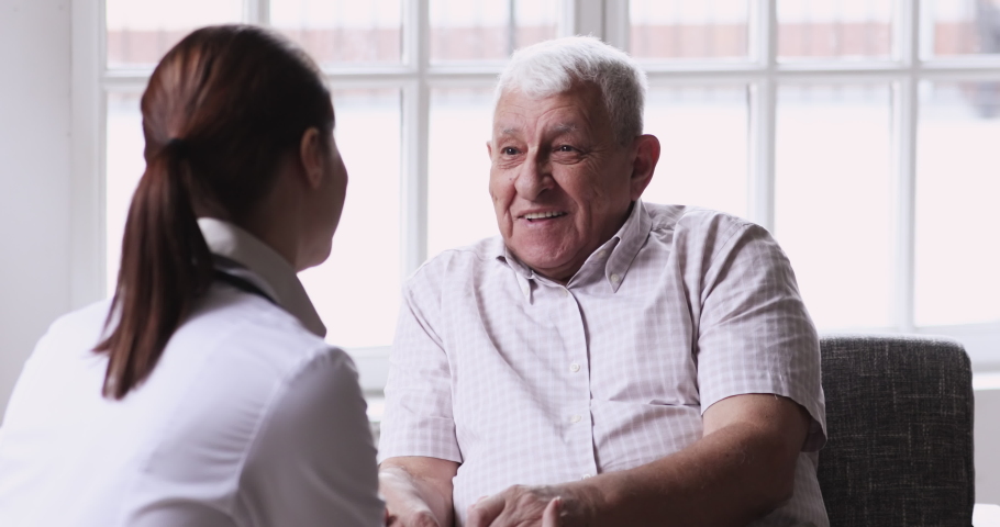 Senior elder man patient talking to caring female doctor physician caregiver at nursing home in hospital holding hands explaining well-being get support and medicare services at medical checkup visit. Royalty-Free Stock Footage #1047837520