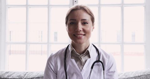 Smiling young female doctor wear white uniform stethoscope consulting online patient via video call looking at camera speaking cam do distance video chat, telemedicine and e-health concept, webcam