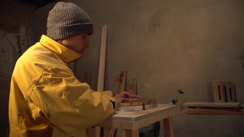 professional worker on an electric grinding machine grinds a wooden part for furniture