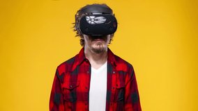 Young man with curly hair using a VR headset and experiencing virtual reality isolated on yellow background