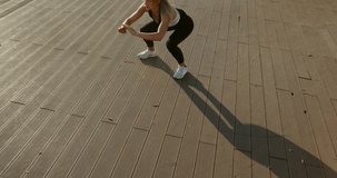 Young woman doing bounce squats on a wooden deck
