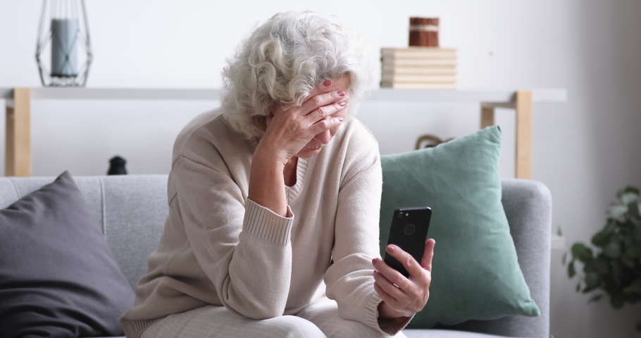 Frustrated senior lady reads bad news in mobile message concept. Sad depressed 70 years old woman looking at smart phone feels shocked. Worried elder female user customer lost money on scam fraud | Shutterstock HD Video #1047850705