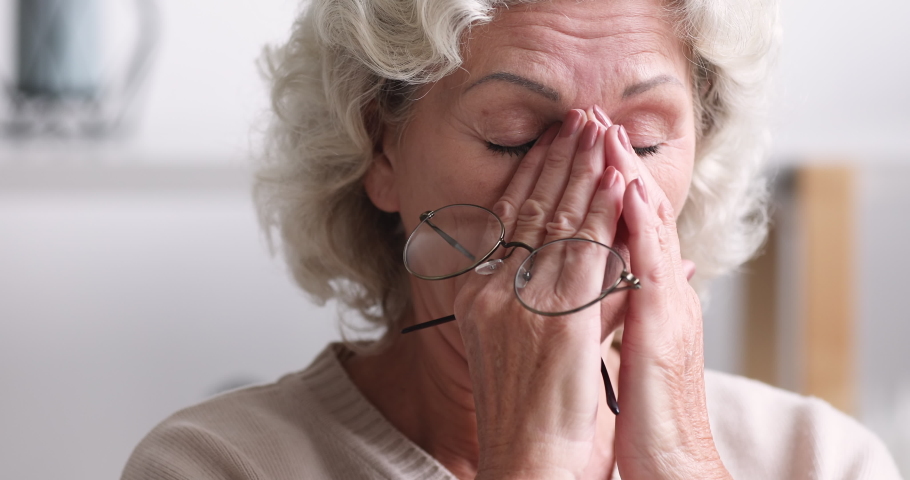 Tired senior adult woman taking off eyeglasses feeling eye strain concept. Exhausted older grandmother holding glasses massaging eyes having headache or bad vision, fatigue problem. Close up view | Shutterstock HD Video #1047858475