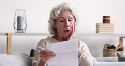 Shocked upset senior woman reading bad news in post mail letter. Frustrated retired grandma holding bill looking worried about dept, troubled with bankruptcy. Unhappy old lady feels bad surprise