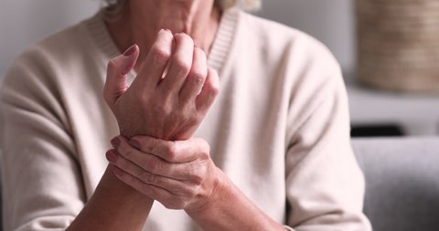 Senior grandmother massaging hand suffering from joint pain. Older woman having rheumatoid arthritis. Elder adult lady touching wrist feeling hurt. Osteoarthritis geriatric disease concept. Close up