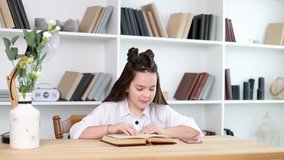 A little girl reads a book in the library, a girl-a diligent student sits and learns school lessons.