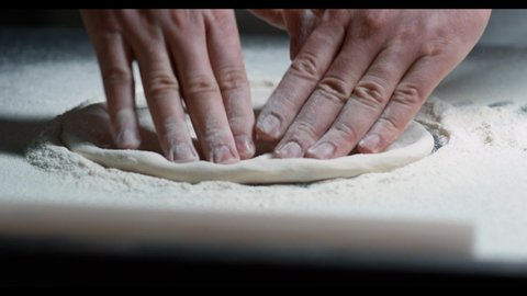 Close up view of hands man doing pizza or pide dough in pastry kitchen traditional baker chef cook food fresh flour dough prepare bake preparation raw table wooden knead recipe homemade slow motion