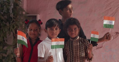 Indian kids raising and wave the Indian national flag or the tiranga tricolor proudly as they salute with pride and positive emotions and look straight at the camera, slow-motion handheld medium shot