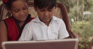 Indian kids learn and operate a large laptop to understand the latest information available online, videos, quiz, e-portal, communicate navigate through the web of internet of things seated outdoors