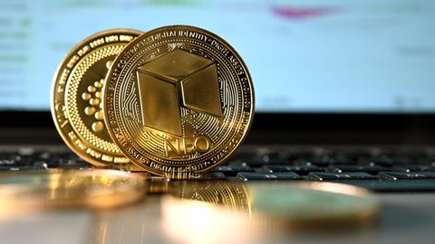 Sideways Pan Of Crypto Currency Shown As Golden Coins With Computer Screen In Background. Iota and Neo Coins.