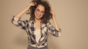 Raw video.Beautiful smiling model with afro curls hairstyle dressed in hipster clothes.Carefree girl posing in studio.Trendy funny and positive woman.She shakes her head and shows surprised emotions 