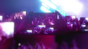 Fans are recording videos on smartphones. A lot of smartphones. Live Stream. Stories. The crowd watches a concert, sings, jumps. Strobing stage lights. Happy people are watching an amazing concert