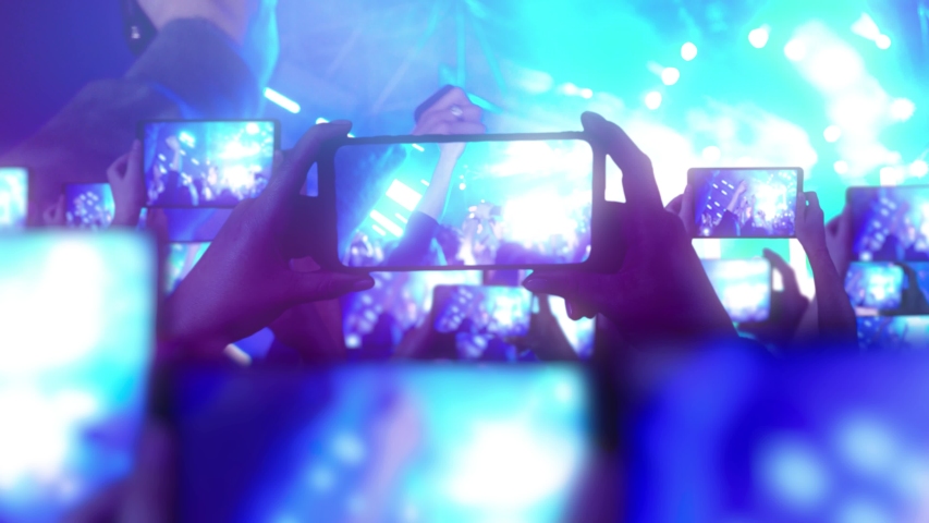 Fans are recording videos on smartphones. A lot of smartphones. Live Stream. Stories. The crowd watches a concert, sings, jumps. Strobing stage lights. Happy people are watching an amazing concert Royalty-Free Stock Footage #1047885718