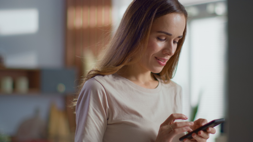 Portrait of attractive woman texting message on smartphone at kitchen. Thoughtful lady using cellphone at home in slow motion. Smiling woman chatting online on mobile phone at domestic kitchen Royalty-Free Stock Footage #1047895561