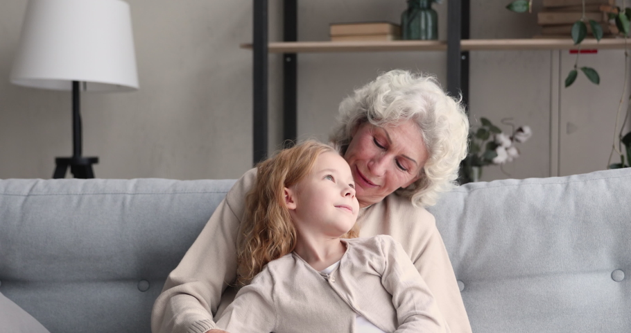Relaxed senior grandma hugging and talking with school child granddaughter at home. Cute small girl grandkid bonding having trust conversation with old grandparent enjoying sweet warm moment together. Royalty-Free Stock Footage #1047898750