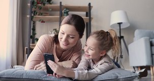 Young happy mom and kid daughter mobile technology users having fun video calling on smartphone. Cute child showing funny app to smiling parent mum. Mother and small girl streaming social media story.