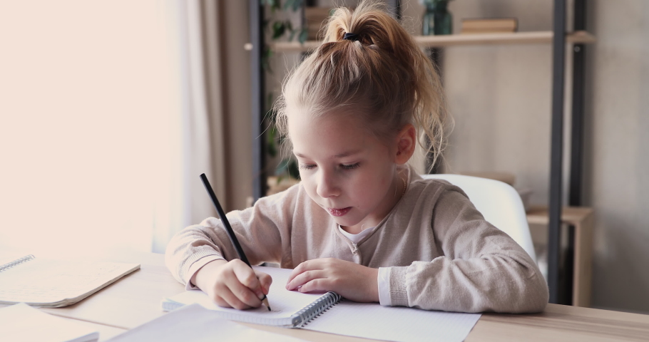 Focused cute smart school child girl studying alone doing writing homework in exercise book sitting at home table. 6-7 years kid learning handwriting making note. Children elementary education concept | Shutterstock HD Video #1047898810