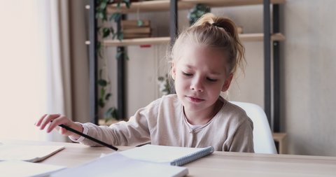 Funny elementary school child girl studies alone talks to herself feels bored, annoyed or tired. Cute lazy 6-7 years kid having difficulty with homework at home. Problem in children education concept