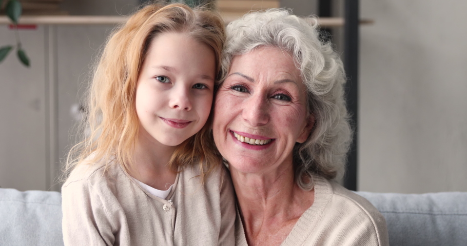 Smiling cute 6-7 years old granddaughter and 70s senior grandmother bonding looking at camera. Funny happy two generations grandparent with girl grandkid family having fun, laughing. Close up portrait | Shutterstock HD Video #1047898858