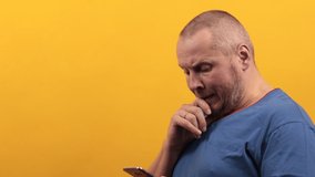 4K video adult man with a beard with different emotions holds a smartphone in his hands, on a yellow background