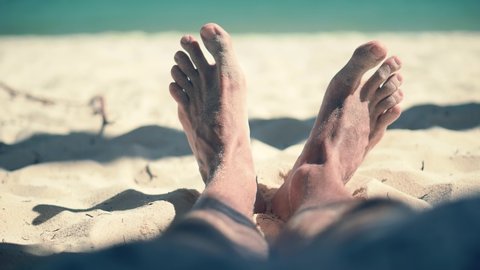 Man Lying On Beach And Moving Legs On Holiday Vacation.Tan Guy Relaxing Sandy Beach In Sunbed On Caribbean Exotic Resort.Legs Man On Beach Sun Lounger Sandy Shore Sunbathing.Happy Healthy Tourist Rest