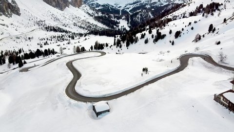 Drone flies over a snowy mountain of the Dolomite above a winding road
