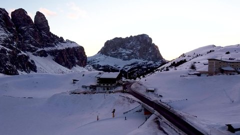 Drone flies over a snowy mountain of the Dolomite above a winding road