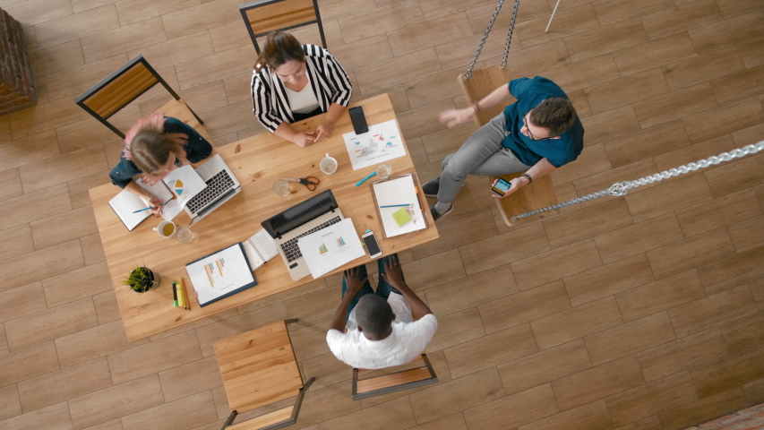Overhead Diverse Business Casual People Meeting for Project Discuss using Laptops. Top View of Startup Employees Team Working in Loft Office with Swing. 4K High Angle Long Gimbal Background Shot | Shutterstock HD Video #1047933454