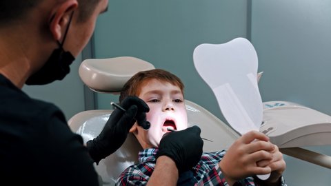 A little boy having a treatment in the modern dentistry - the boy holding a mirror and looking what's doing the dentist