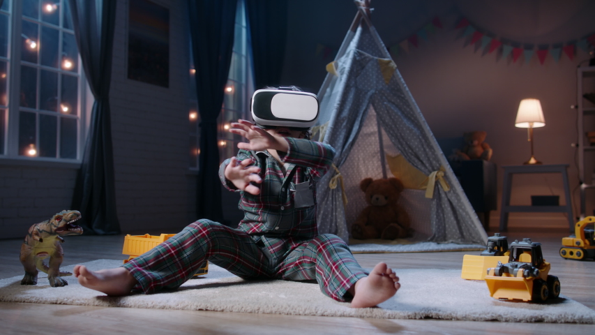Cute little boy wearing pajamas is diving into virtual reality world before bedtime, using vr 3d headset, playing video games - modern technology concept 4k footage Royalty-Free Stock Footage #1047950962