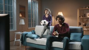 Funny asian male siblings with curly hair spending time together, watching soccer game on tv and emotionally reacting. Authentic father and son enjoying their hobby - family time concept 4k footage