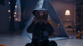 Funny little kid wearing pajamas is putting on virtual reality headset to dive into video games before bedtime , getting lit and having fun 4k footage