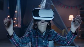 Funny little kid wearing pajamas is putting on virtual reality headset to dive into video games before bedtime , getting lit and having fun 4k footage