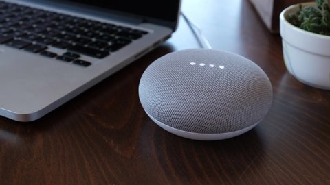 Istanbul, Turkey - January 20 2020: Google home mini smart speaker with built in Google Assistant. speaker stand on working table near the laptop and slide camera movement