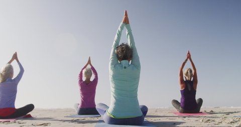 Rear view of a group of Caucasian female friends enjoying free time on a beach by the sea on a sunny day together, meditating with arms in the air  in slow motion Video Stok