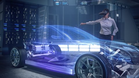 Automotive Female Professional Engineer working on design of Electric Car using Futuristic Augmented Reality Headset with Holographic Technology at High-tech facility. Electric car chassis.