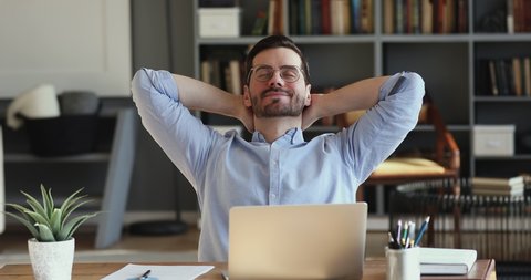 Relaxed businessman takes break to relieve stress. Satisfied happy male employee meditating sitting at workplace desk holding hands behind head. Office worker finished work feels peace of mind concept