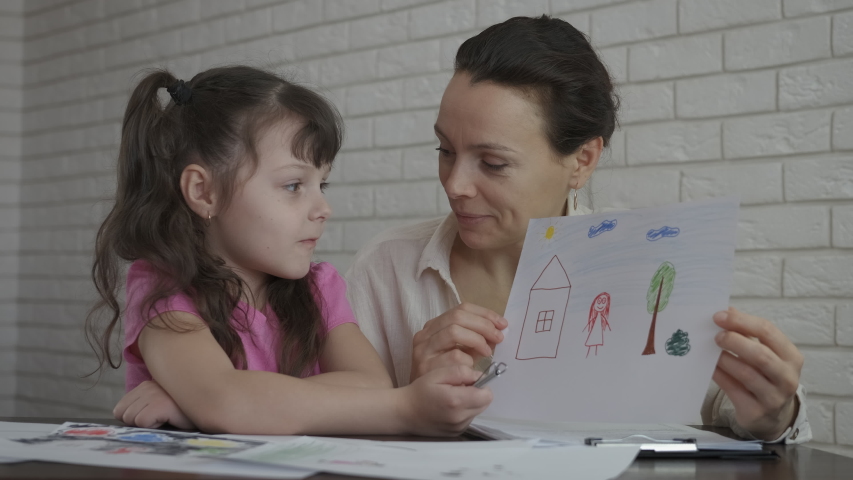 The child is a psychologist. A little girl shows her drawings to a psychologist. | Shutterstock HD Video #1047984511