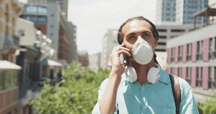 Front view of a mixed race man with long dreadlocks out and about in the city on a sunny day, standing in the street wearing a coronavirus mask and using a smartphone in slow motion.
