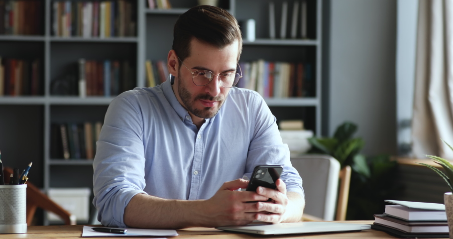Mad unhappy businessman feeling annoyed using smart phone. Angry businessman having problem with mobile spam message. Male user frustrated by low battery or bad signal concept sitting at office desk. | Shutterstock HD Video #1047988531