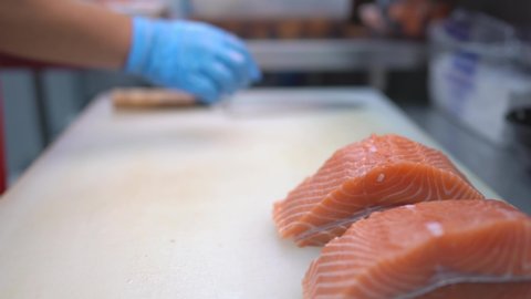 Close up scene of a chef's hand cutting salmon into fillets, preparing for salmon steak,  concept of salmon hygiene food processor, healthy food processing, the seafood industry, chef guide cuts.