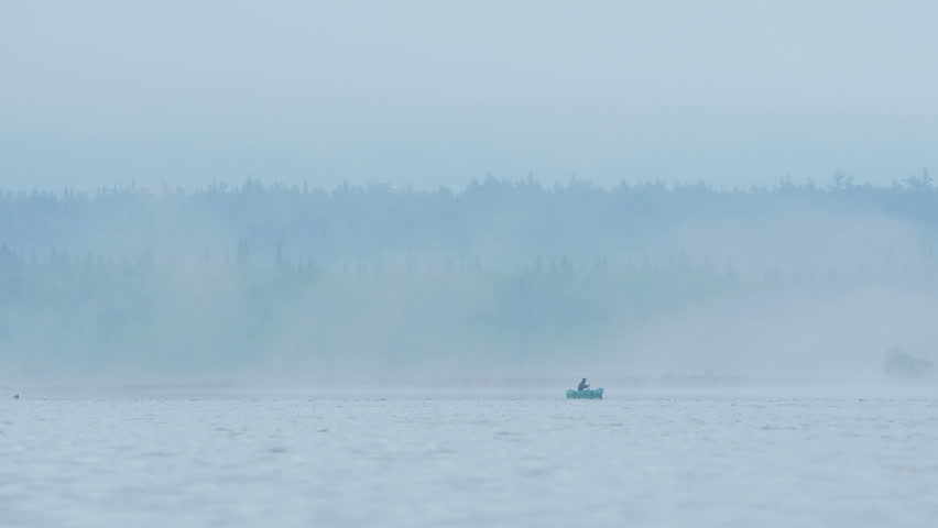 Fisherman in the boat on the foggy forest lake.