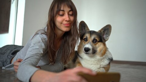 beautiful young girl hugging and kissing her cute curious corgi dog and taking selfie using phone