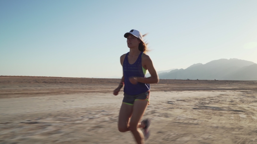 View of young motivated girl jogging in dry desert at sunrise