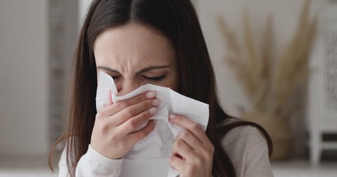 Ill allergic young woman sneezing in tissue blowing running nose. Sick girl got flu concept or caught cold, having allergy symptoms. Unhealthy lady suffer from seasonal virus disease. Close up view