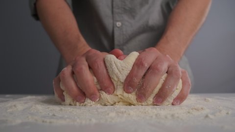 A male baker in a shirt kneads and forms the dough. Male hands with the dough. Close-up.