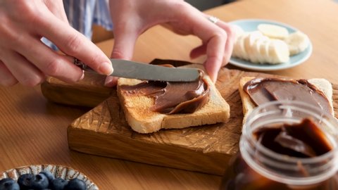 Spreading chocolate nut spread on toasted bread. Woman preparing tasty breakfast or lunch sandwich with chocolate nut butter