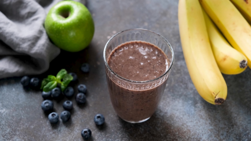 Healthy raw fruit and chocolate protein smoothie. Female hand stirring smoothie in glass with paper cocktail straw. Healthy fitness vegan lifestyle concept